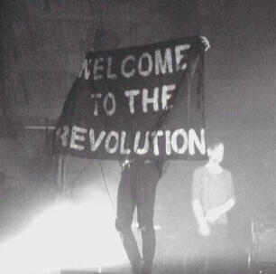 Achillean couple holding a paper with "our love is not a crime" and two hearts.