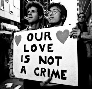 Achillean couple holding a paper with "our love is not a crime" and two hearts.