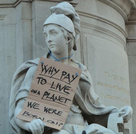 Imagem de uma estátua de mármore de Athena, segurando uma placa escrito "Por que pagar para viver no planeta em que nascemos?".